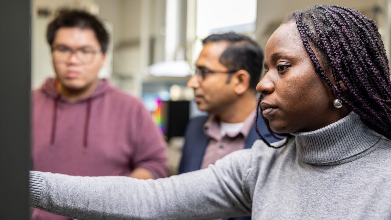 Three people work in a precision timing lab at The University of Alabama.